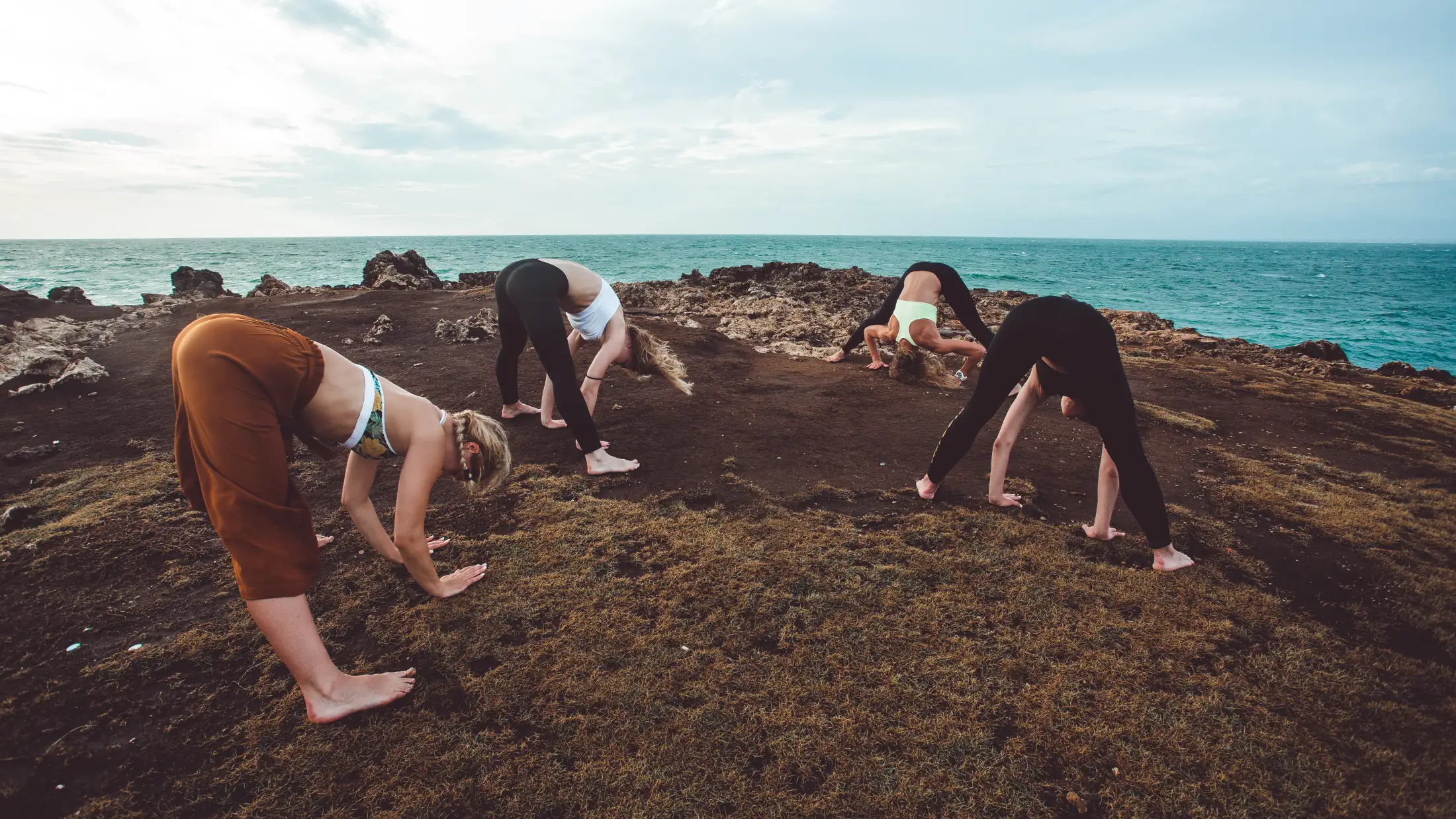 Cuatro personas haciendo un estiramiento de yoga al borde de un acantilado junto al mar